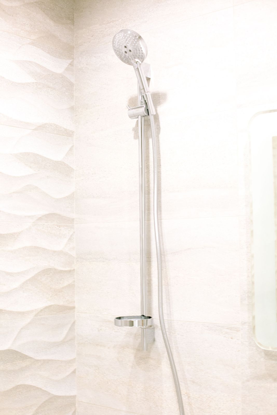 Chrome handheld shower on a slide rail with soap ring against light textured wall tiles